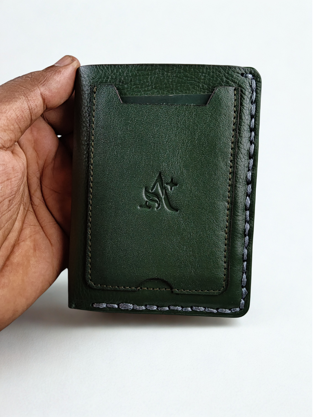 Hand holding dark green genuine leather vertical bi-fold wallet with outer card pocket