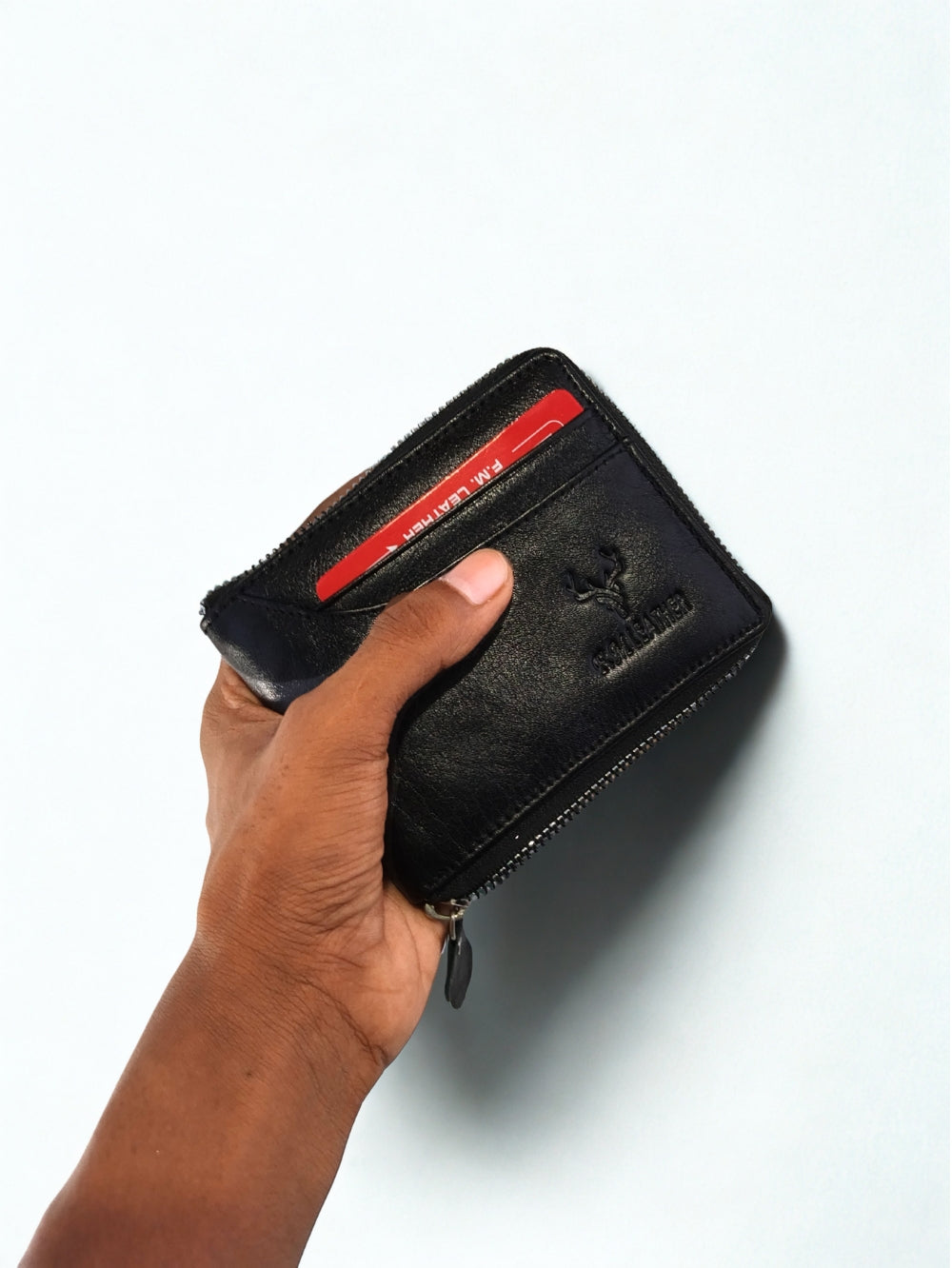 Hand holding black full grain leather zip-around men's wallet